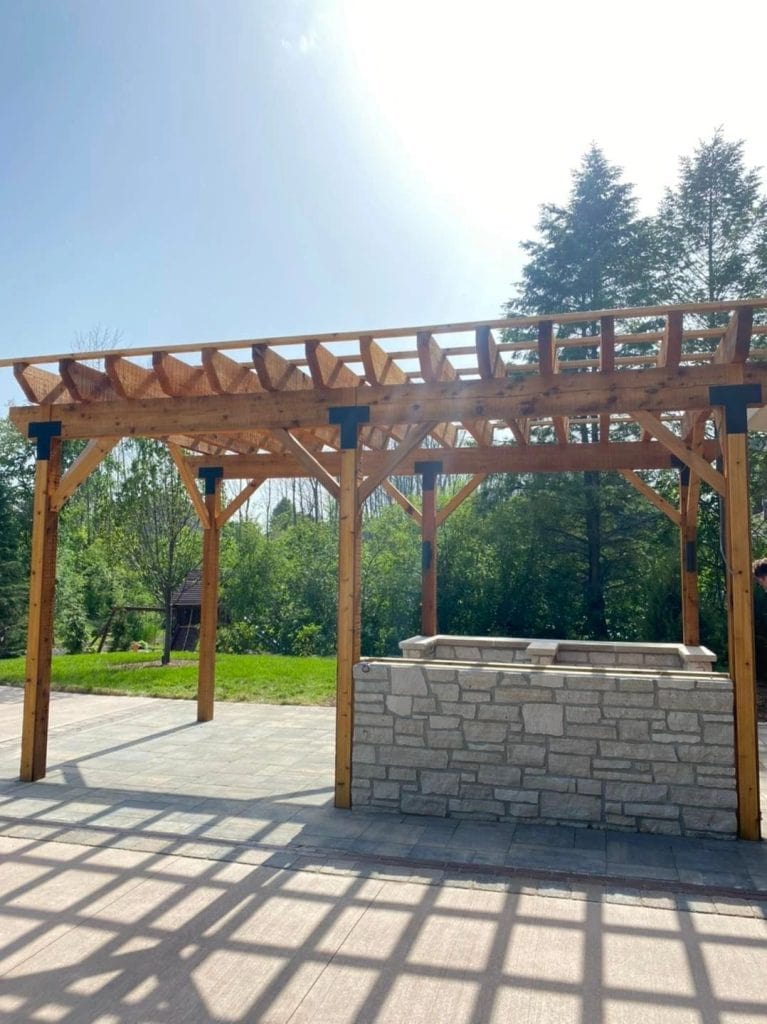 Beautiful outdoor pergola construction with wooden beams and stone countertop, perfect for garden gatherings and outdoor living spaces.