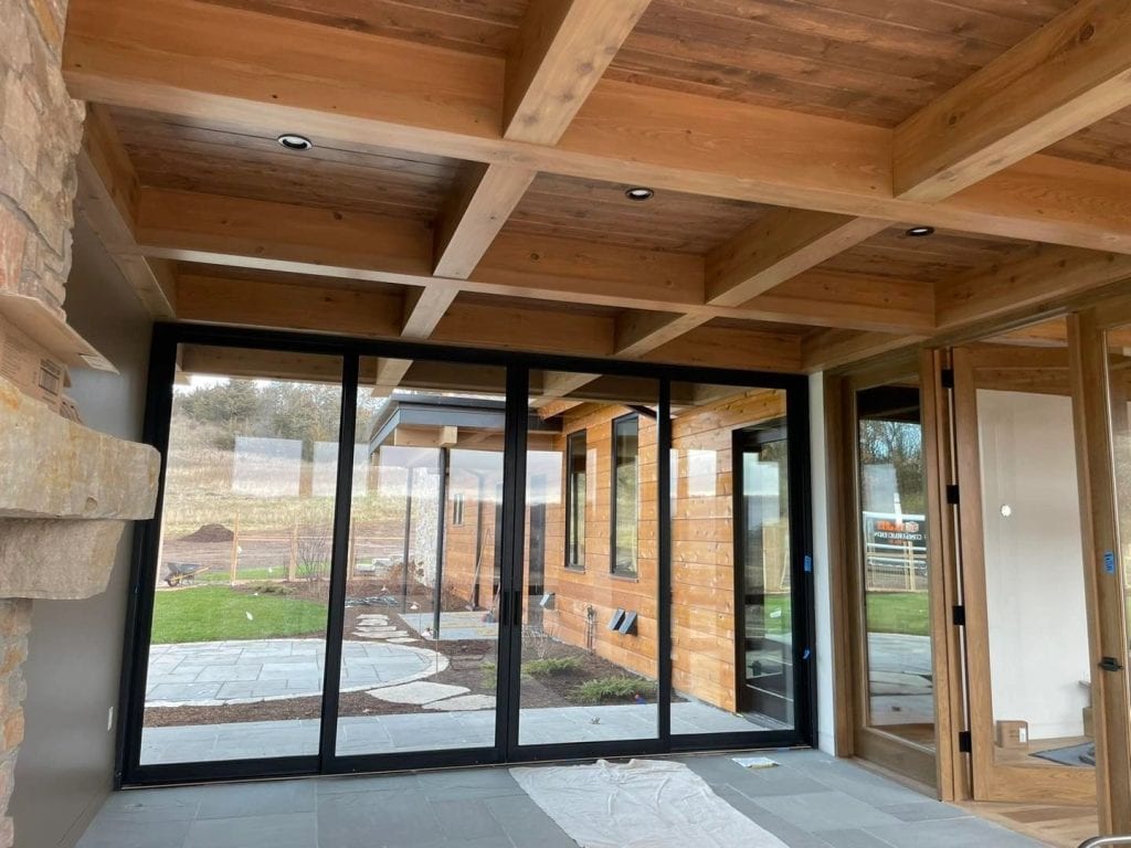 Elegant glass patio enclosure with wooden beams and outdoor landscaping, showcasing high-quality painting and decorating work by Hi-Tech Painting and Decorating.