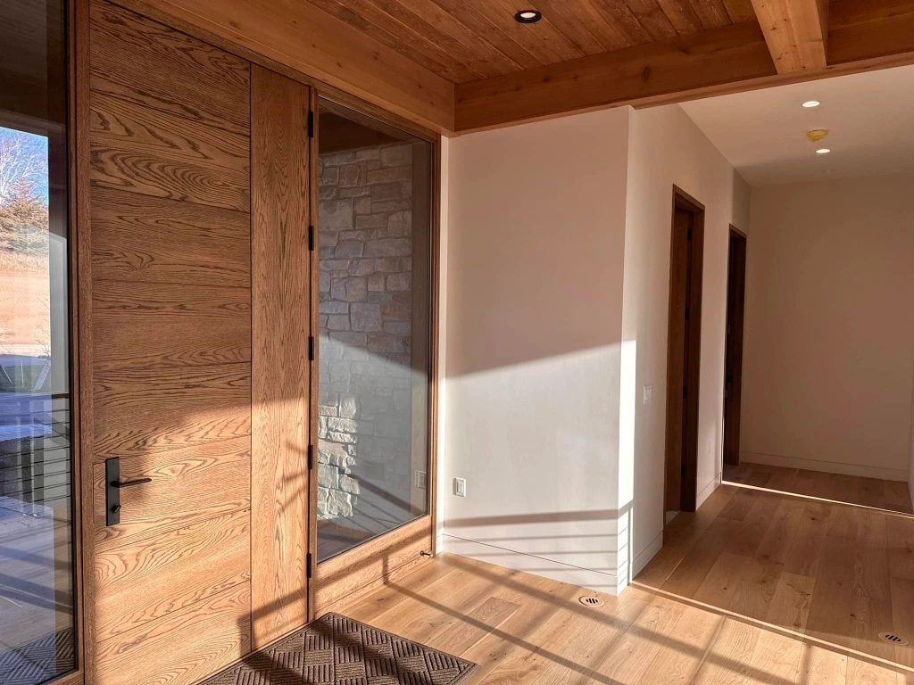 Bright and inviting interior space featuring wooden doors, a glass panel, and hardwood flooring illuminated by natural sunlight. Perfect for showcasing professional painting and decorating services.